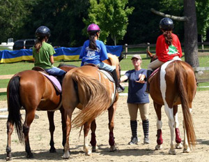 A riding staffer teaches basics to several campers.