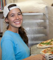 A kitchen staffer caries two fresh pizzas from the oven